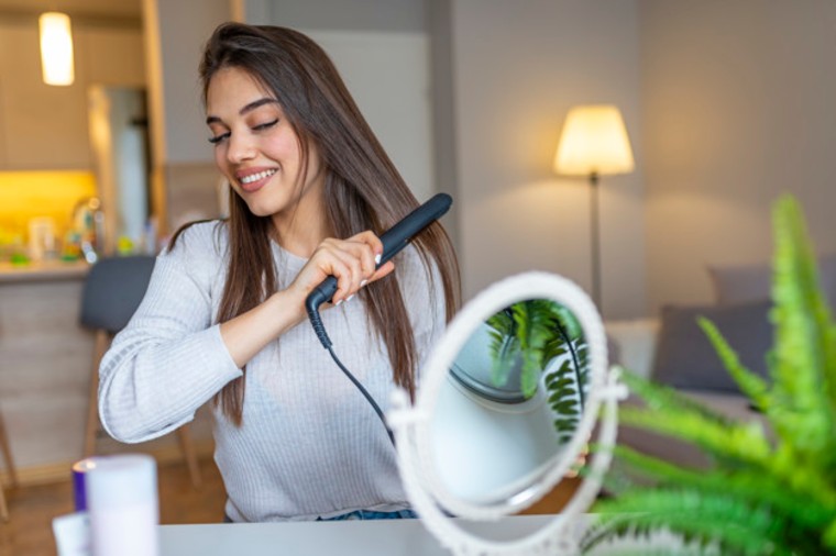 beautiful-girl-is-using-hair-straightener-smiling-while-looking-into-mirror-home-smiling-woman-straightening-hair-with-hair-straightener