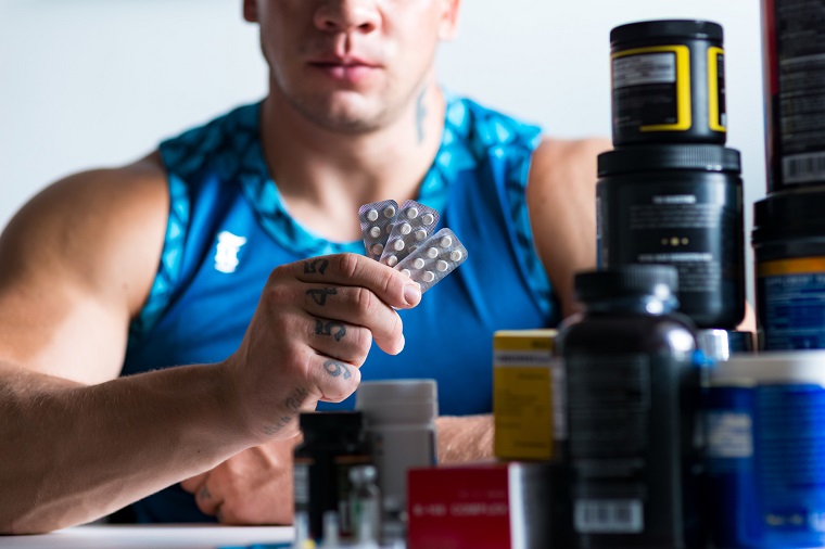 close up of pills in hands of a professional bodybuilder holding them while sitting at the table