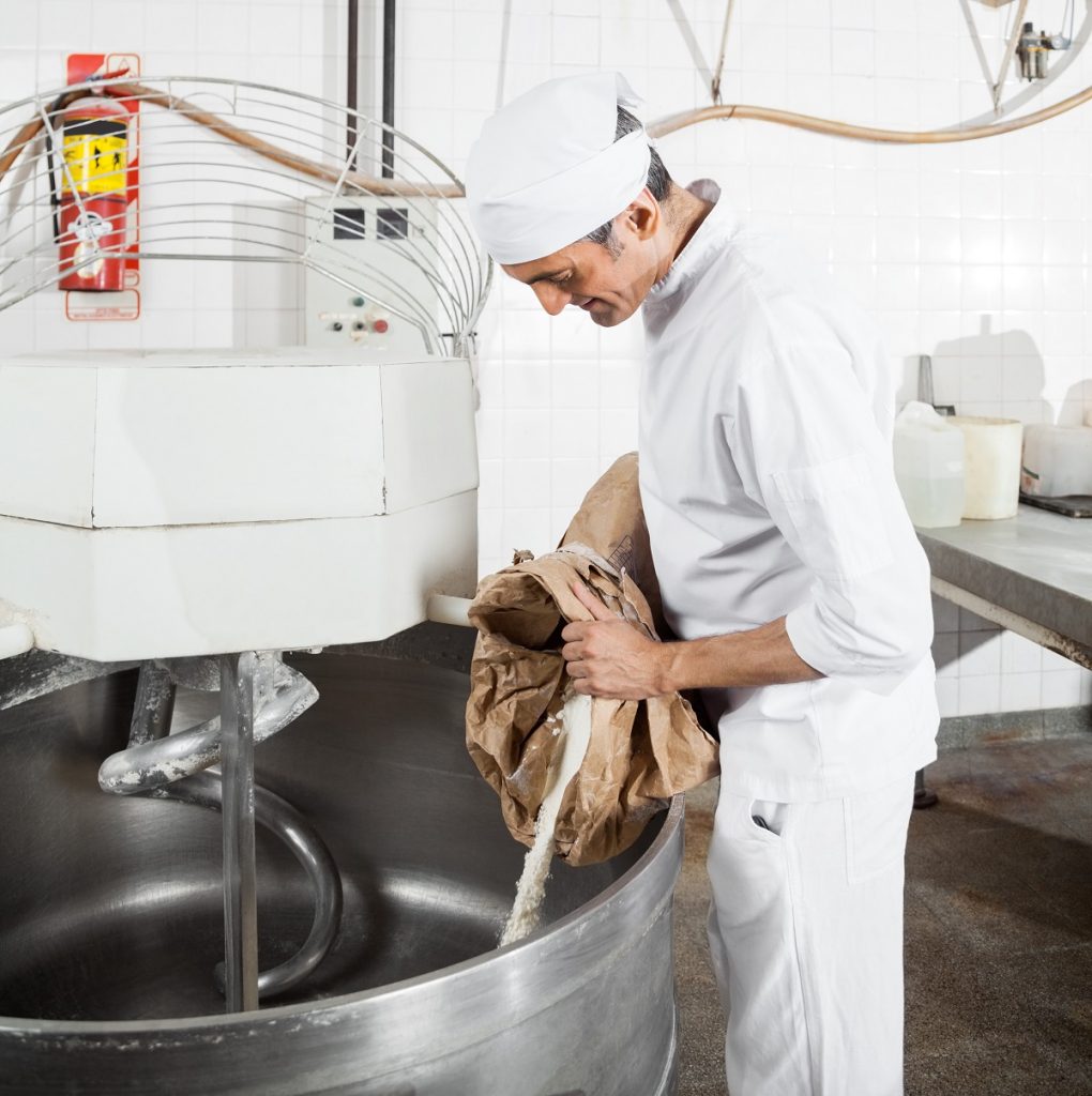 Mature Baker Pouring Flour In Mixing Machine