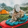 Woman sitting on a sleeping bag next to the lake