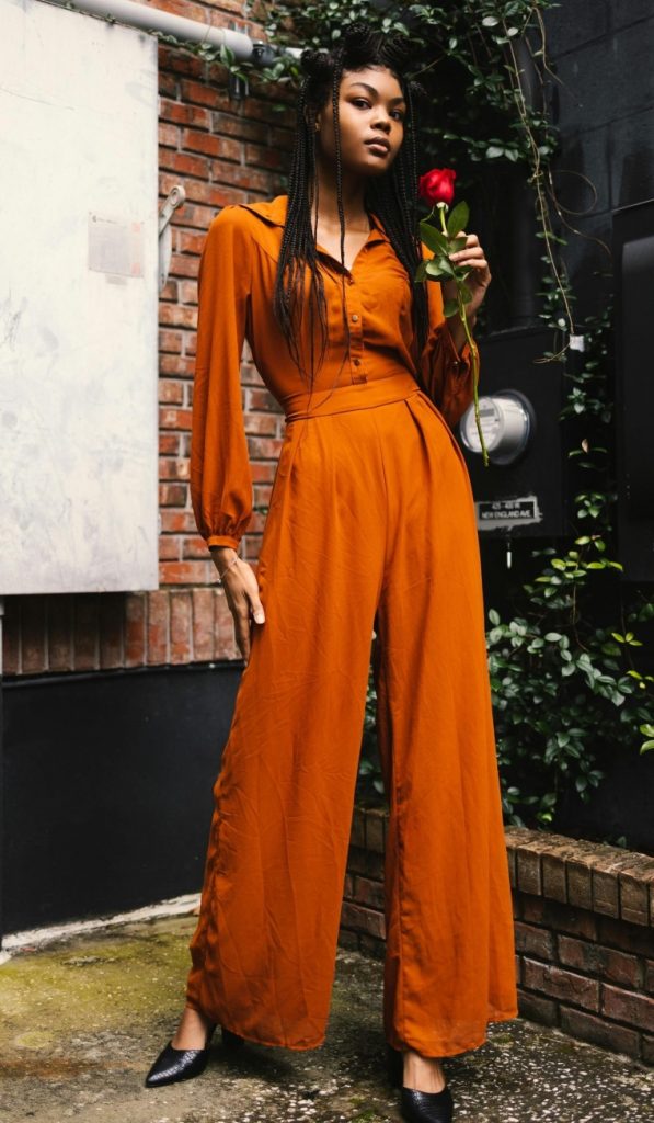 woman wearing orange jumpsuit for ladies, standing and holding a rose