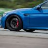 Close-up of a blue BMW sports car showing motion blur, focused on the front wheel with a performance brake system by Harrop