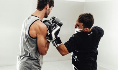 Two boxers practicing punches in a bright gym, with one wearing grey sleeveless top and Venum boxing gloves receiving a punch from the other in black attire and black and white Venum gloves.