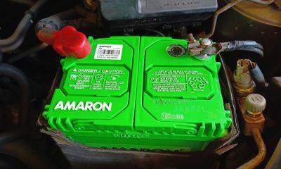 Amaron car battery installed in a vehicle engine compartment, highlighting the brand logo and safety warnings.
