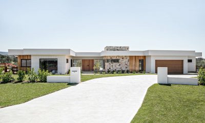 Modern single-story house with a wide driveway leading to a garage and front entrance, surrounded by a well-manicured lawn.