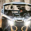 Person in a Can-Am off-road vehicle navigating through a forest trail.